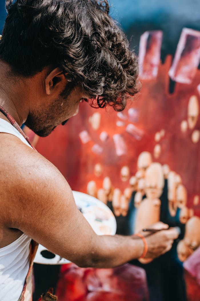 Male artist painting a colorful abstract artwork on a canvas outdoors during the day.