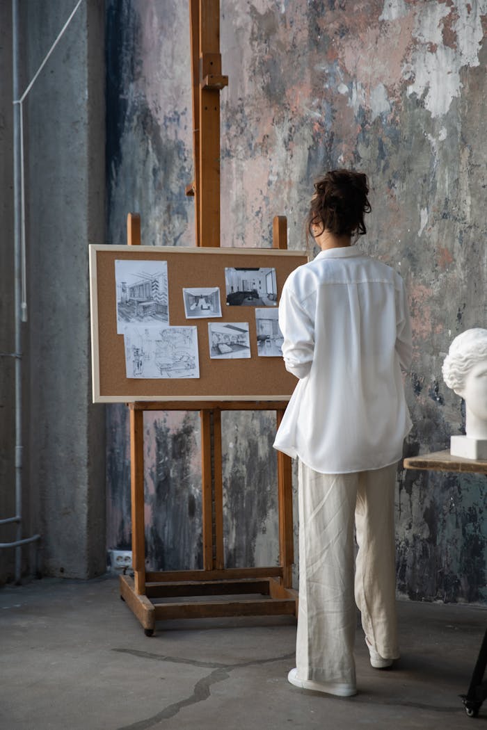 A woman stands in an art studio, examining sketches pinned on a corkboard. Creative workspace.